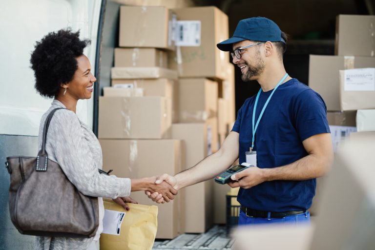 Happy courier handshaking with African American woman while delivering her a package.